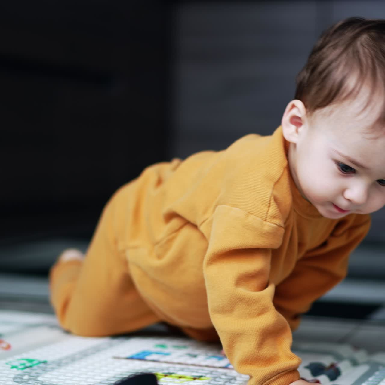 Nice little baby boy crawling by the floor and looking carefully at the carpet. Toddler playing indoors. Blurred backdrop