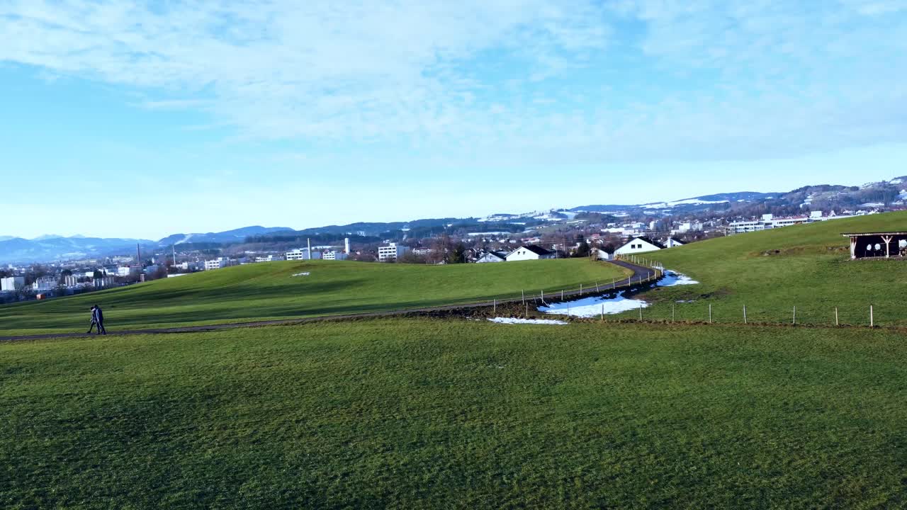 무인 항공기가 고도를 높이고 백그라운드에서 도시와 알프스를 드러내면서 산책하는 두 사람