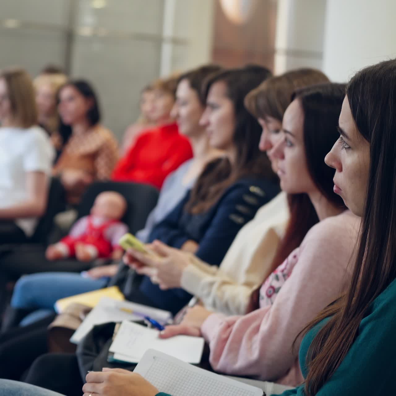 Beautiful women sitting in a row during the conference. Young people with copybooks listen to the public seminar indoors.