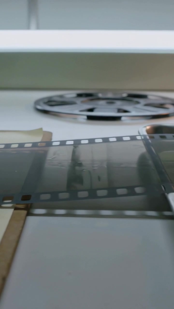 Vertikal video: Glidende U-formet værktøj presser 35mm film på lysbord, udglatter til inspektion