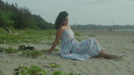 Attractive-indian-woman-is-sitting-on-the-beach-in-a-blue-dress at-sumemer