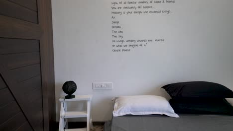 minimalist bedroom interiors with traveling quote on the white wall above the gray bed with black and white pillows, small black lamp on the white side table - tilt down shot