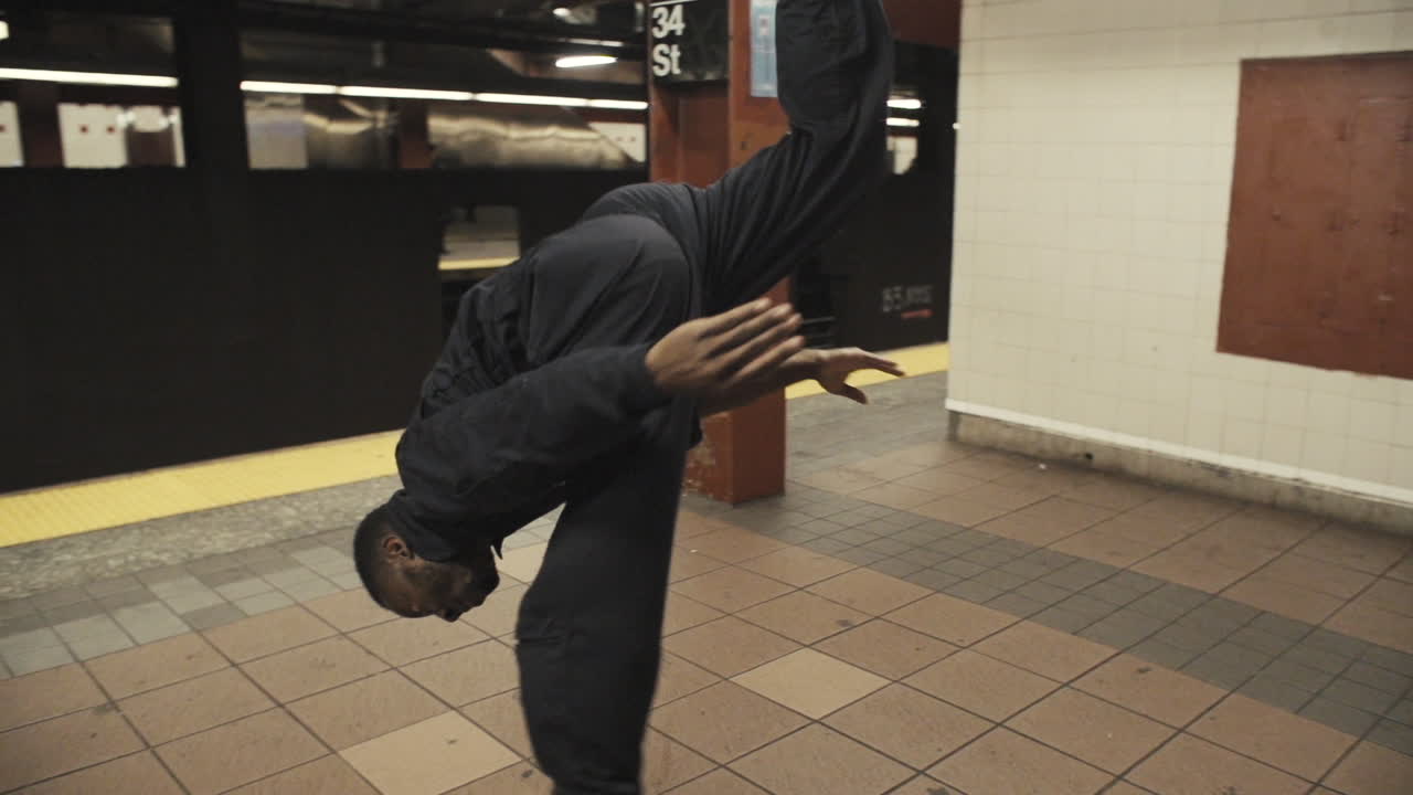 Janitor dancer flips on subway platform as steadicam wraps around as train pulls away