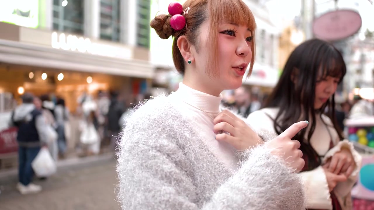 混雑した歩道で、トレンディな日本のストリートファッションを身につけた2人の若い女性が話し、笑っている。