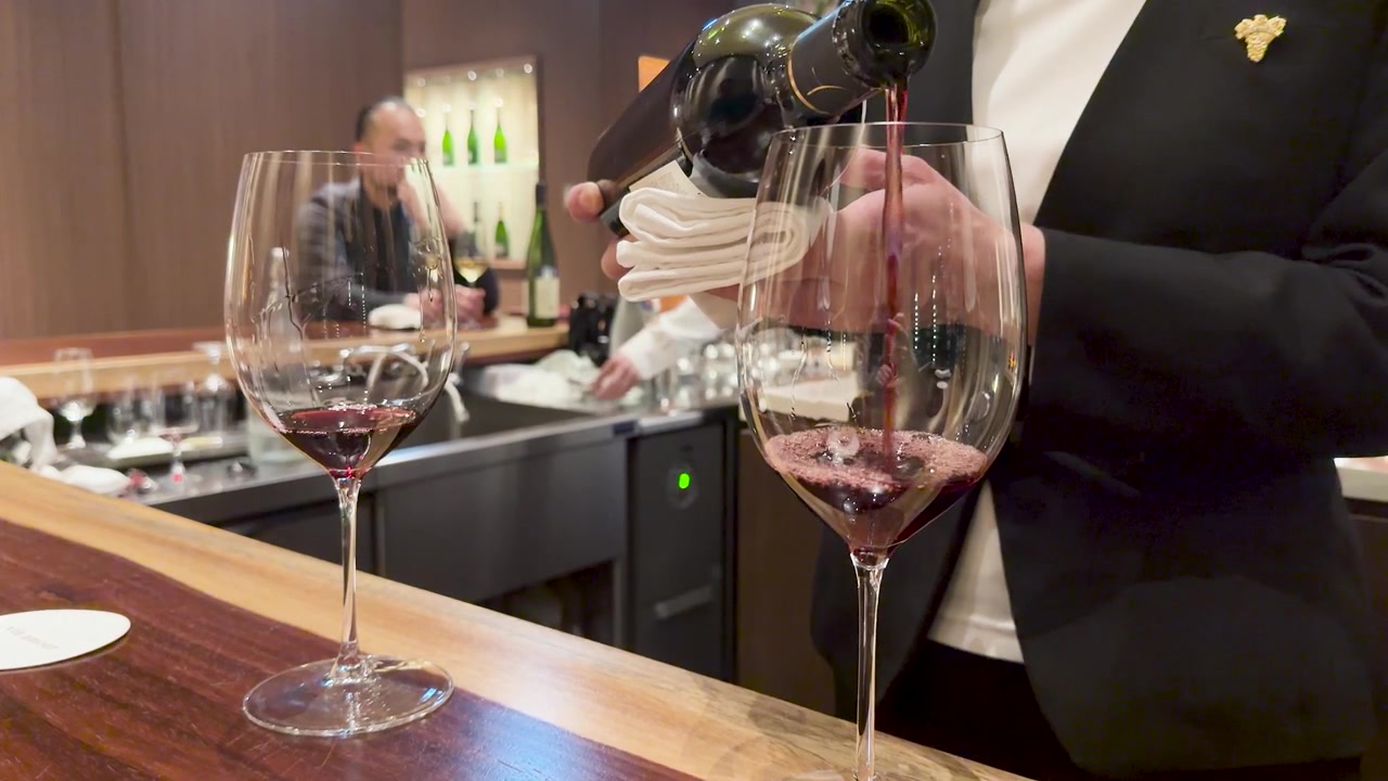 Een sommelier in pak schenkt rode wijn uit een fles in een groot glas