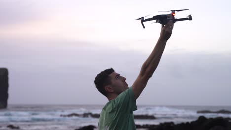 man stands on coast, raises his arm and catches modern drone with right hand