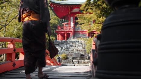 Slide-shot-of-a-person-wearing-a-Hakama-walking-over-a-bridge-in-a-Japanese-garden-in-Kyoto,-Japan-4K-slow-motion