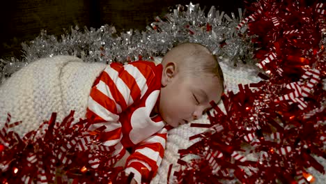 Adorable-Cute-2-Month-Old-Indian-Baby-Boy-In-Festive-Outfit-Sleeping-Surrounded-By-Red-And-Silver-Tinsel