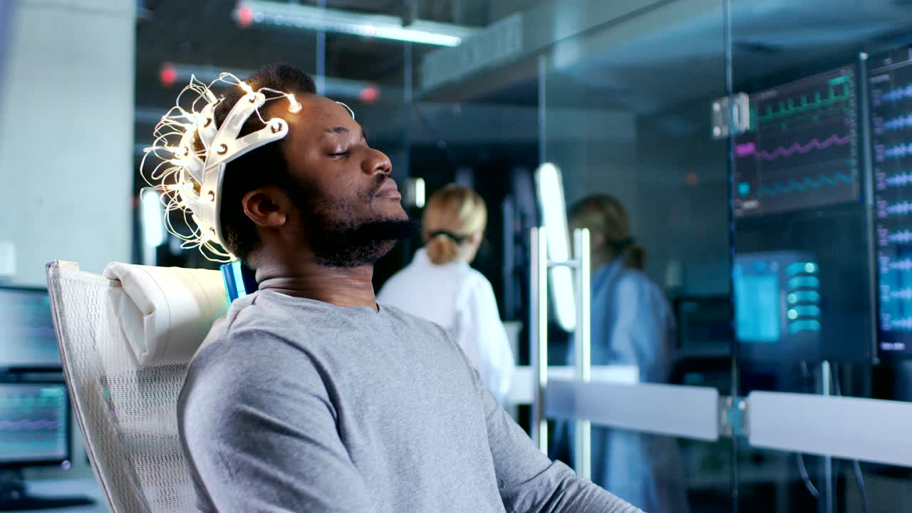 un hombre con auriculares de escaneo de ondas cerebrales se sienta en una silla mientras un científico con una tableta supervisa el proceso. en el laboratorio de estudio moderno del cerebro, los monitores muestran la lectura de eeg y el modelo cerebral.
