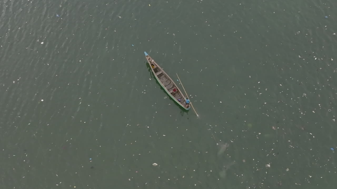 imágenes aéreas de un bote largo que viaja lentamente a través del agua con basura a su alrededor