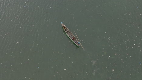 Imágenes-Aéreas-De-Un-Bote-Largo-Que-Viaja-Lentamente-A-Través-Del-Agua-Con-Basura-A-Su-Alrededor