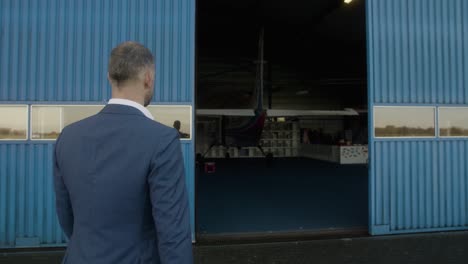 Business-man-walks-towards-plane-in-hangar