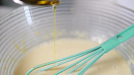 Close-Up-view-of-female-hands-adding-oil-from-the-spoon-to-the-bowl-preparing-dough-and-mixing-the-ingredients-using-whisk