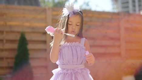 a little girl in a dress is blowing soap bubbles in the backyard on a sunny summer day