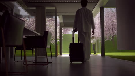 person with suitcase in modern house overlooking cherry blossom garden