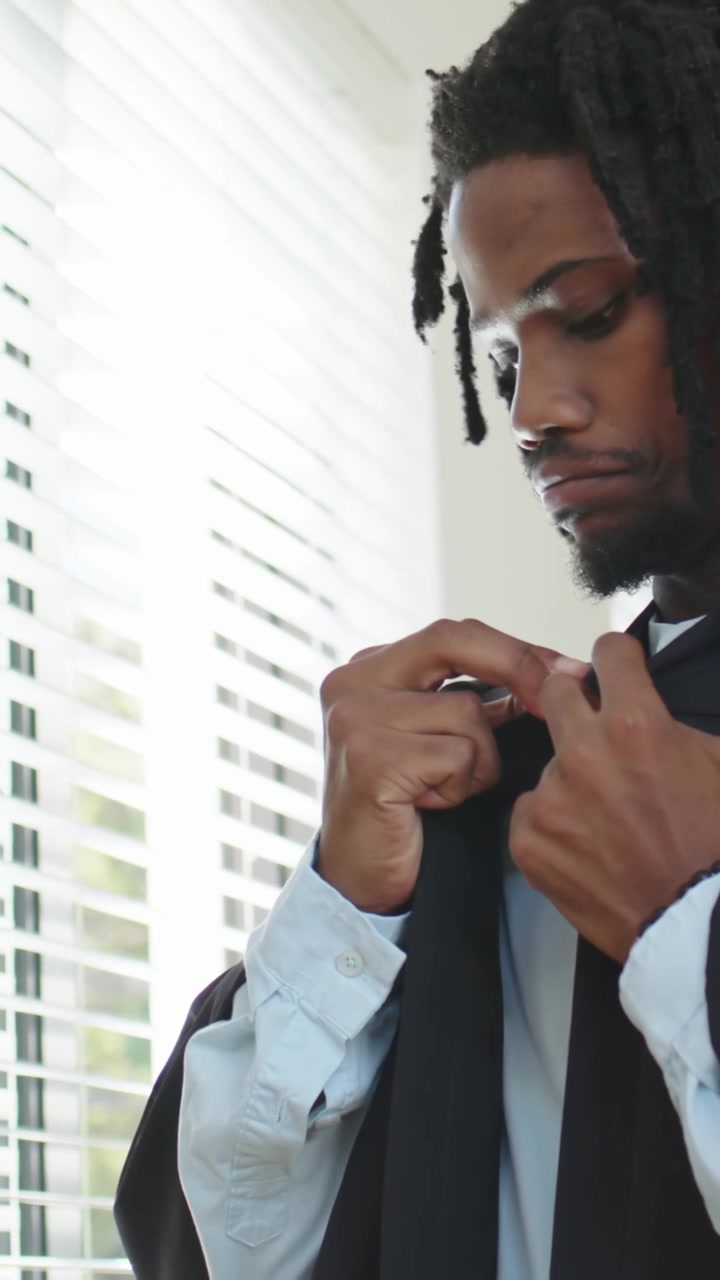 Vertical video: Preparing for event, man fastening robe clasp by blinds, adjusting tie, copy space