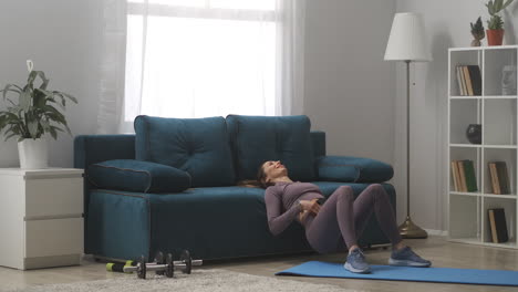 ama de casa está haciendo ejercicios para los músculos abdominales en casa apoyándose en el sofá en la sala de estar levantando las caderas ejercicio doméstico en auto-aislación
