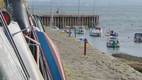 camera slowly pans along stone dock with moored fishing boats in scottish harbour, daylight