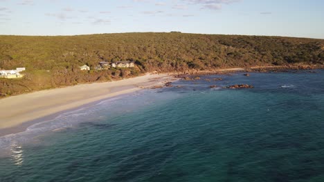 drone aerial over a beautiful blue beach next to a national park full of green trees