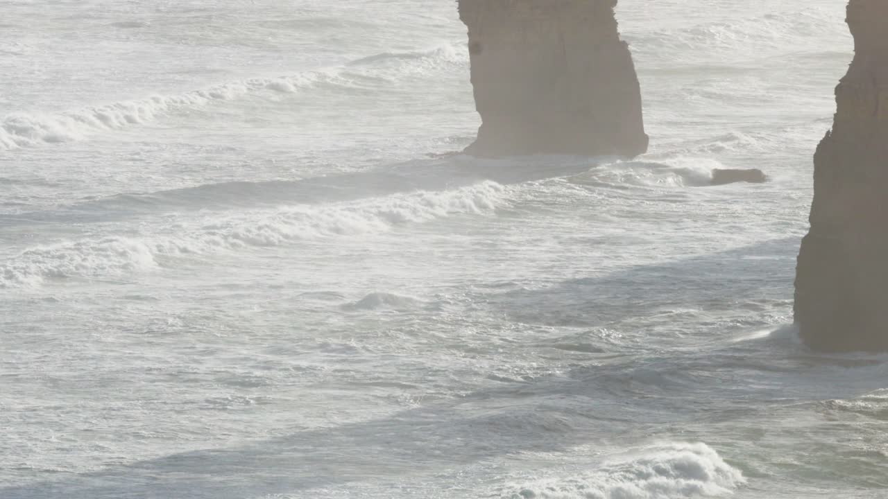 Dynamic ocean waves crash against the iconic limestone stacks of the Twelve Apostles under soft, natural lighting