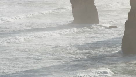 dynamic ocean waves crash against the iconic limestone stacks of the twelve apostles under soft, natural lighting