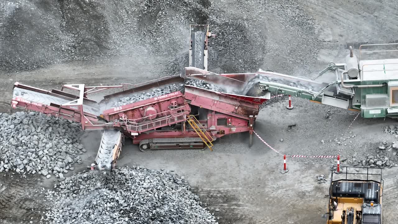 Aerial panning shot of excavator placing rocks into conveyor belt sorting machine