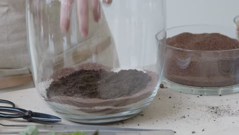 a young woman creates a small ecosystem in a glass terrarium - preparing the decorative layer - nature preservation concept - close-up