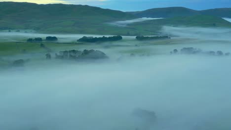 Misty-English-countryside-with-slow-pan-revealing-patchwork-fields,-hills-and-mountains-at-sunrise