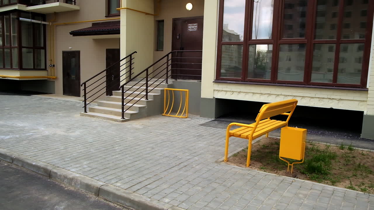 Exterior of an apartment building with a yellow bench and trash can
