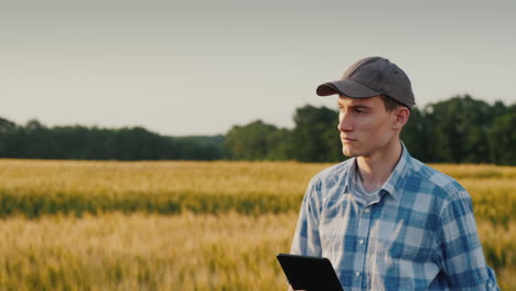 Un-Joven-Agricultor-Con-Una-Tableta-En-La-Mano-Camina-Por-Un-Campo-De-Trigo