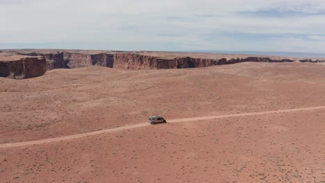 aerial, van life camper van on a road trip driving on dry red desert road in utah