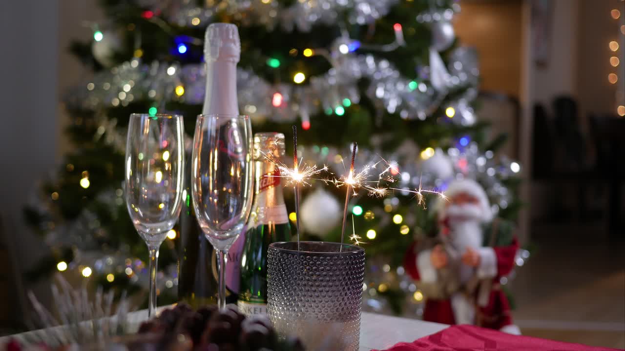 Due bicchieri vuoti e una bottiglia di champagne accanto a stelline luminose ardenti in un portacandele su un tavolo, sullo sfondo di un albero di Natale decorato.