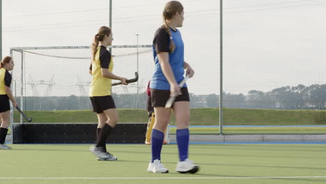 female hockey players competing on field, focused on scoring goal