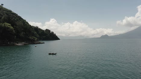 Isolated-man-on-boat-floating-on-Atitlan-lake-with-San-Pedro-volcano-in-background,-Guatemala