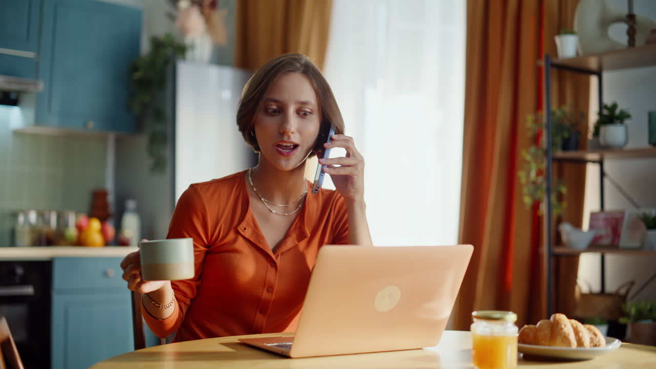 Glad freelancer, der taler i mobiltelefon og holder en kaffekop i køkkenet - nærbillede