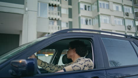 guy sitting automobile looking on city road. man leaning window car