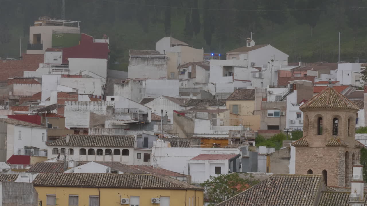 Un camion dei pompieri rosso con luci di emergenza blu attive attraversa le case bianche del centro storico di Jaén durante un'emergenza incendio.