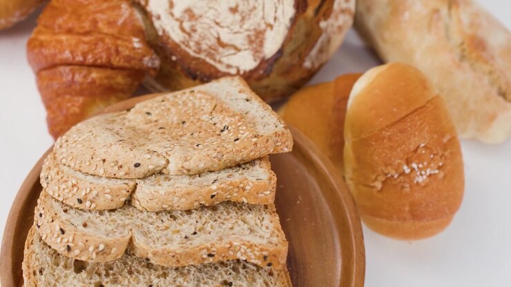 Slow rotation of sliced whole grain bread, croissants, and baguettes under bright studio lighting.