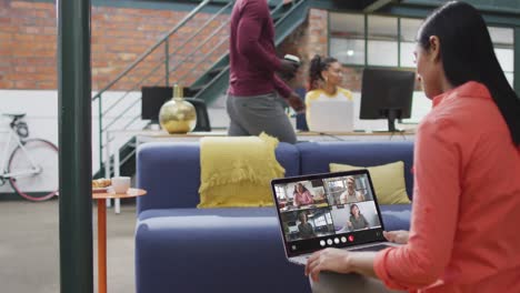 Biracial-woman-using-laptop-for-video-call,-with-diverse-business-colleagues-on-screen