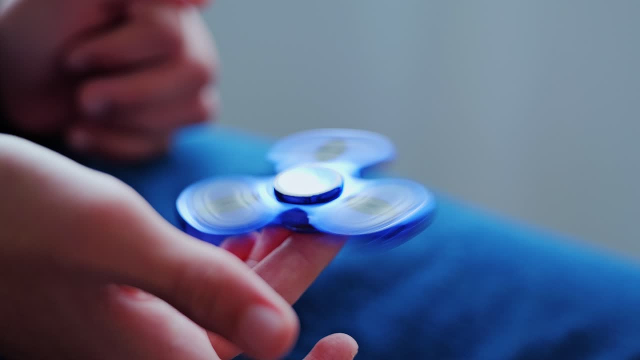 Blauer Fidget Spinner dreht sich sanft auf dem Finger eines Kindes im Haus und zeigt eine ruhige Bewegung