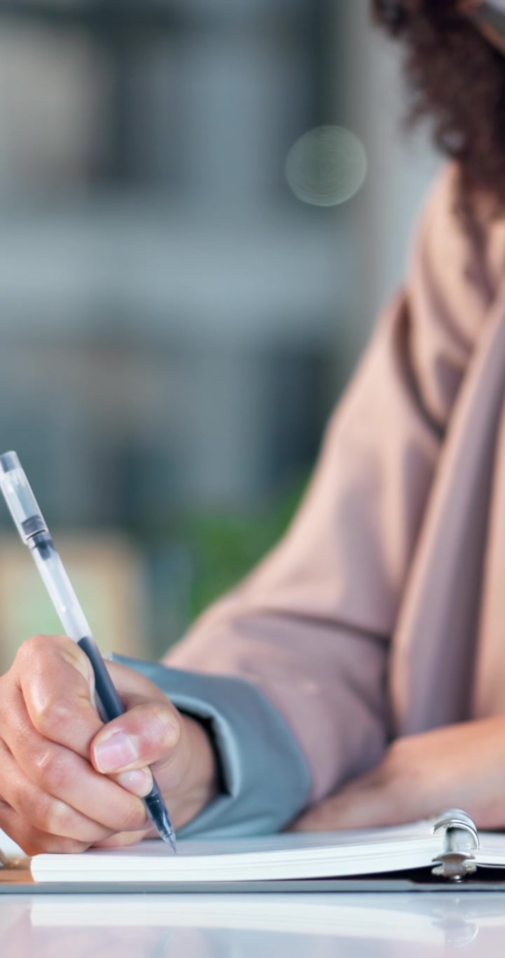 Close-up of a Person Writing in a Notebook at a Desk