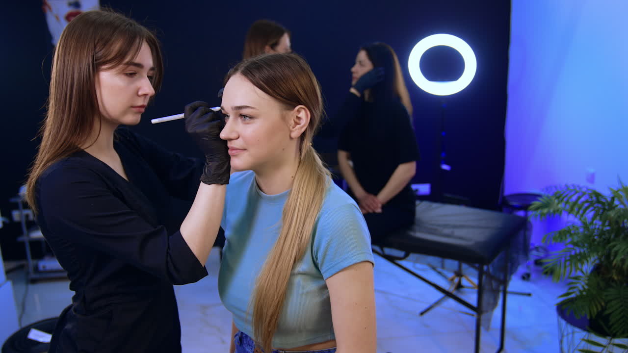 Female clients having eyebrow make up in the beauty salon. Cosmetologist marks the lines with white pencil.