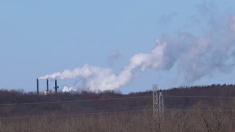 Huge-industrial-chimneys-emerging-from-behind-a-thick-forest-releasing-white-smoke-into-the-atmosphere