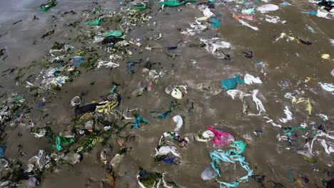 aerial backwards ground level view of beach full with garbage