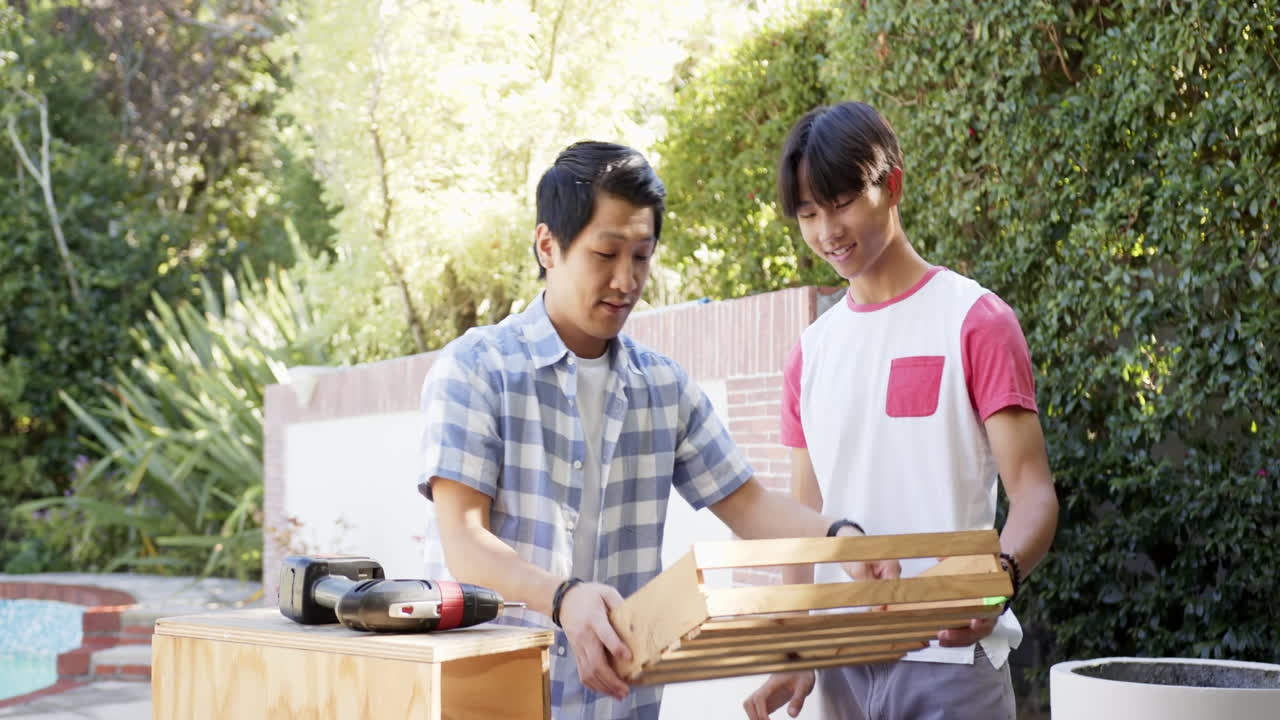 Building wooden project, asian father and son collaborating and using drill outdoors