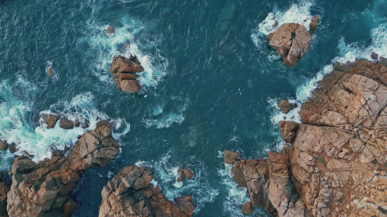 Mare che bagna la costa rocciosa, vista dall'alto. Incredibili onde azzurre che si infrangono su scogliere aspre