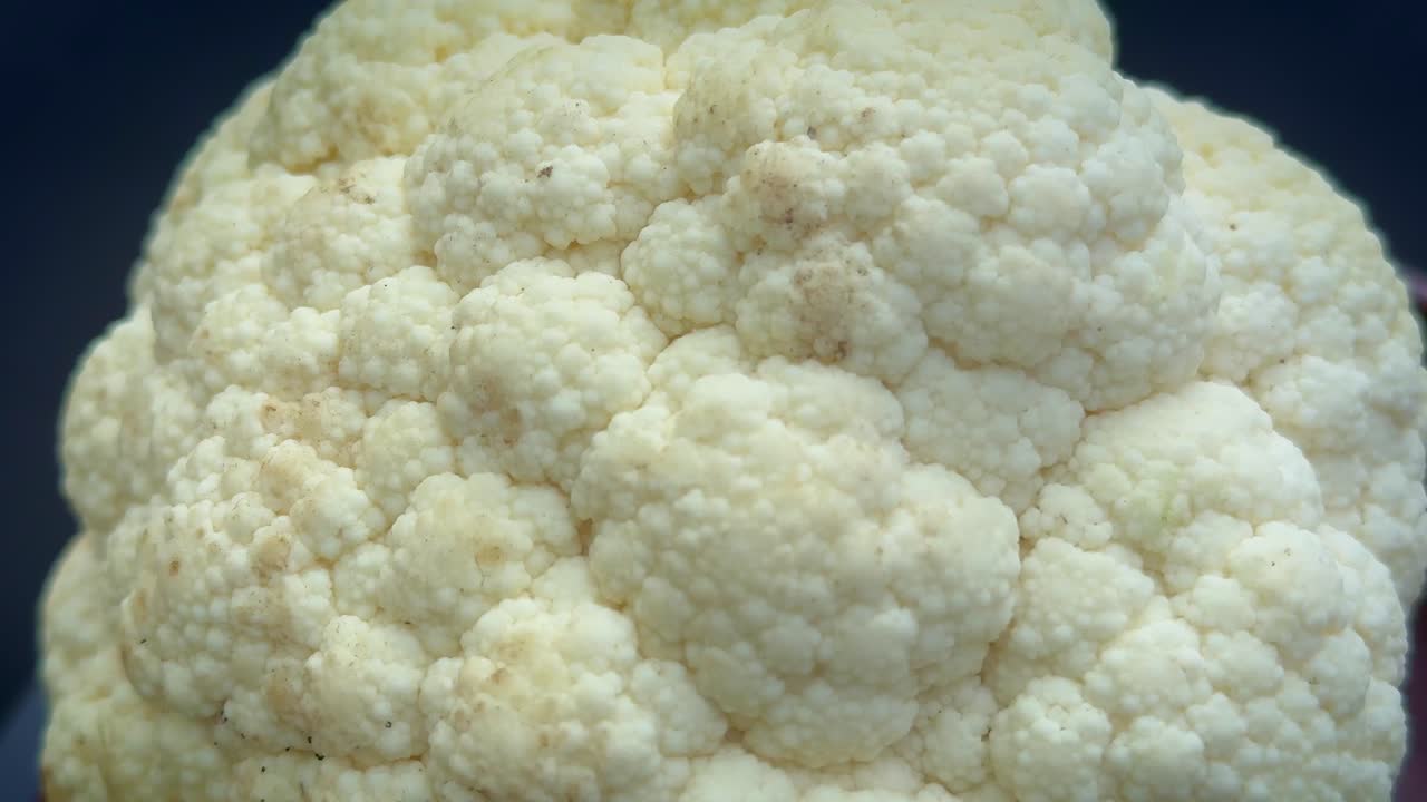 Primo piano su giradischi di rosette di cavolfiore fresco che ruotano delicatamente, con una texture bianco crema che cattura la luce soffusa mentre il movimento leggero rivela i dettagli naturali