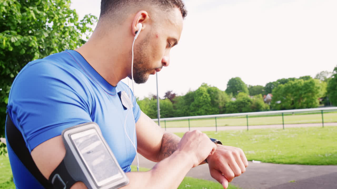 Man at track puts on headphones, sets watch app, starts run