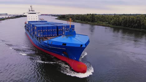 toma en órbita de un enorme barco portacontenedores panda azul con viento de cola navegando en el río oude maas, países bajos