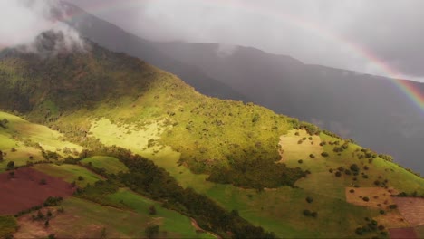 Vista-Aérea-Panorámica-De-Un-Doble-Arco-Iris-Adornando-La-Ladera-Y-El-Paisaje-Montañoso-En-Ecuador